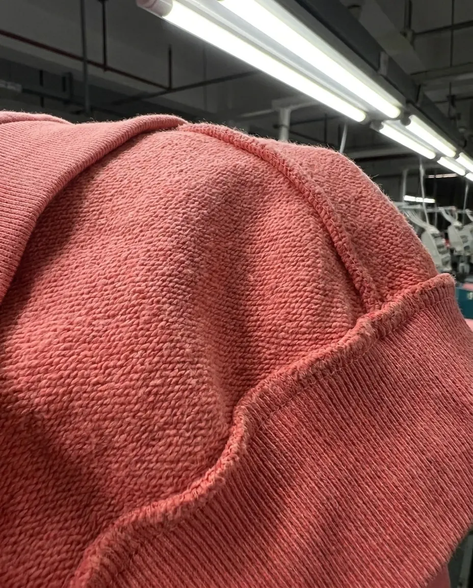 Close-up of a coral hoodie shoulder seam showing heavyweight loopback fabric texture